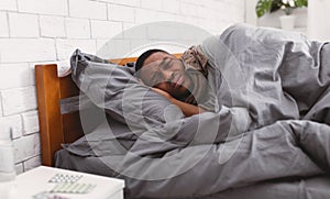 Unhappy Sick Black Guy Lying Wrapped In Blanket In Bedroom