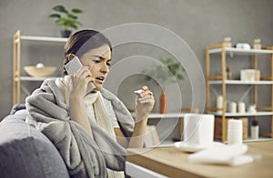 Unhappy sick woman sitting on sofa, looking at thermometer and calling her doctor