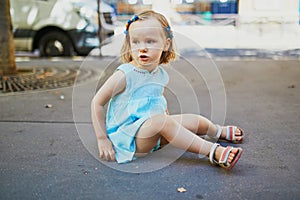 Unhappy and stubborn toddler girl sitting on the floor outdoors