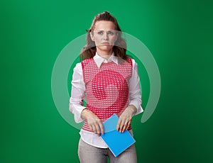Unhappy student woman with blue notebook isolated on green