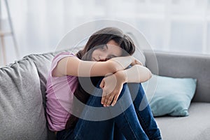 Unhappy teen girl feeling depressed or desperate, sitting on couch at home, suffering from problem or teenage depression