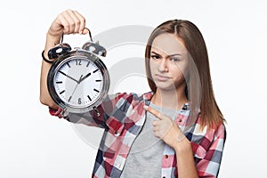 Unhappy teen girl holding big alarm clock pulling discontent face