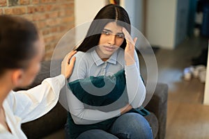 Unhappy teen lady having problem, hugging pillow and talking with friend who showing compassion and trying to appease