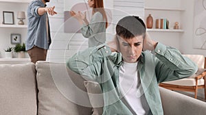 Unhappy teenage boy covering ears while his parents arguing on background. Problems at home