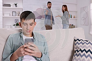 Unhappy teenage boy scrolling through phone while his parents arguing on background. Problems at home