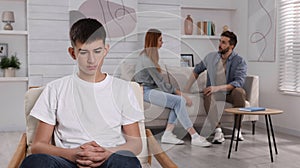 Unhappy teenage boy sitting in armchair while his parents arguing on background. Problems at home