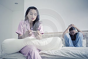 Unhappy teenage couple with pregnancy test on bed