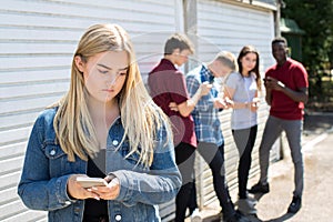 Unhappy Teenage Girl Being Bullied By Text Message Outdoors