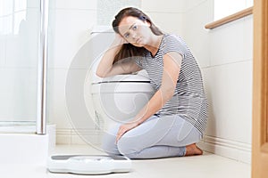 Unhappy Teenage Girl Sitting On Floor With Bathroom Scales