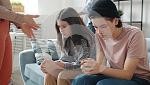 Unhappy teenagers brother and sister sitting on couch while parents yelling punishing kids at home