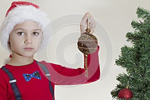 Unhappy tired boy in Santa cap holding xmas toy near Christmas tree