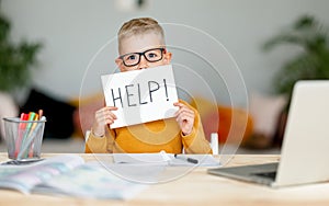 Unhappy tired child  boy student holds a sign HELP while doing homework at home