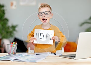 Unhappy tired child  boy student holds a sign HELP while doing homework at home