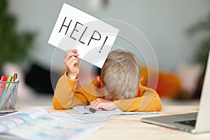 Unhappy tired child  boy student holds a sign HELP while doing homework at home