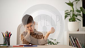 Unhappy tired european small kid suffers from learning difficulties show banner with inscription help
