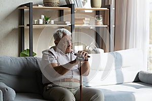 Unhappy tired senior man with walking cane resting on sofa.