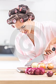 Unhappy wife with hair curlers cuts onion with a knife