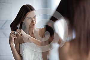 Unhappy woman brush tangled long hair in bathroom