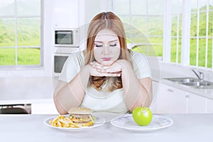 Unhappy woman choosing apple or burger