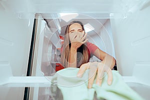 Unhappy Woman Cleaning Stinky Dirty Fridge with a Cloth photo