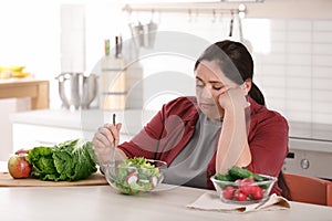 Unhappy woman eating vegetable salad at table
