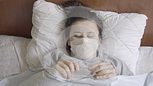 Unhappy woman in face mask taking temperature. Top view of female patient measuring body temperature with thermometer