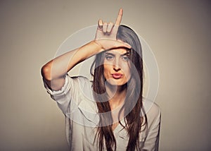 Unhappy woman giving loser sign on forehead, looking at you, disgust on face