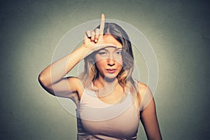 Unhappy woman giving loser sign on forehead, looking at you, disgust on face