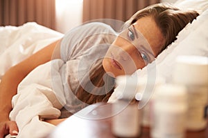 Unhappy Woman Looking At Medication On Bedside Table