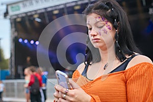 Unhappy Woman Looking At Mobile Phone Trying To Meet Friends At Outdoor Summer Music Festival 