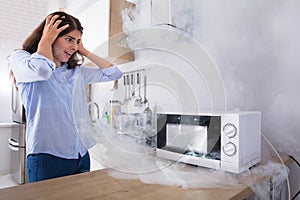 Unhappy Woman Looking At Smoke Emitting Through Microwave Oven