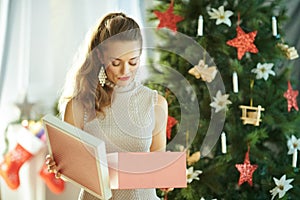 Unhappy woman with opened Christmas gift near Christmas tree