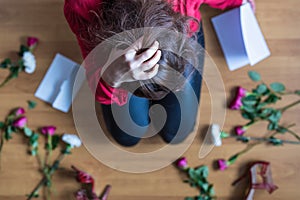 Unhappy woman sitting on the floor among scattered flowers and reading letter. Broken relationships in bad Valentine`s day