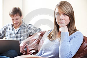 Unhappy Woman Sitting On Sofa As Partner Uses Laptop