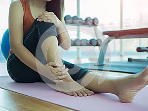 Unhappy woman sitting on the yoga mat with ankle injury