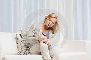 Unhappy woman suffering from pain in leg at home