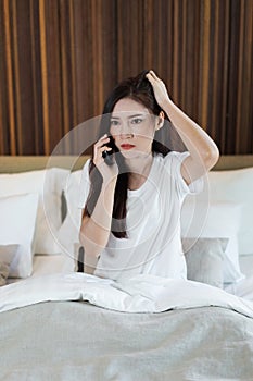 Unhappy woman talking on mobile phone on a bed