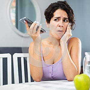 Unhappy woman talking on mobile phone at home