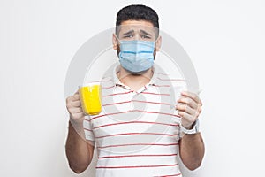 Unhappy worry sick man with surgical medical mask standing and holding yellow cup with white tissue, drink hot tea, has flu, sick