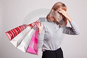 Unhappy young Asian woman with shopping bags and credit card.