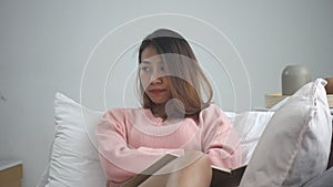 Unhappy young asian woman studying at home reading an sms or text message on her mobile phone with lying on the couch at home