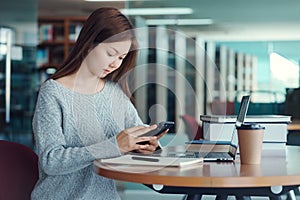 Unhappy young asian woman talking on mobile phone while reading book in library