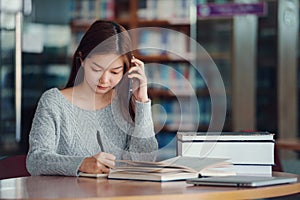 Unhappy young asian woman talking on mobile phone while reading book in library