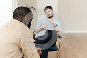 Unhappy young black man having session with professional psychologist at mental health clinic. Professional