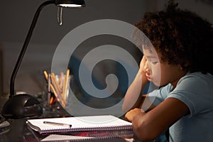 Unhappy Young Boy Studying At Desk In Bedroom In Evening