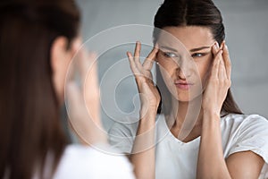 Unhappy young brunette woman dissatisfied with first wrinkles.