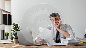 Unhappy young businessman feeling bored and stressed at work looking at laptop with hopeless expression while sitting in