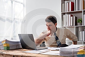 Unhappy young businessman feeling bored and stressed at work looking at laptop with hopeless expression while sitting in