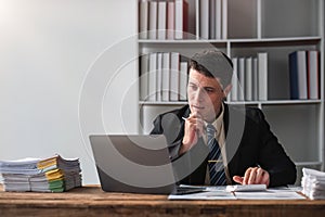 Unhappy young businessman feeling bored and stressed at work looking at laptop with hopeless expression while sitting in