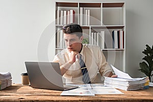 Unhappy young businessman feeling bored and stressed at work looking at laptop with hopeless expression while sitting in